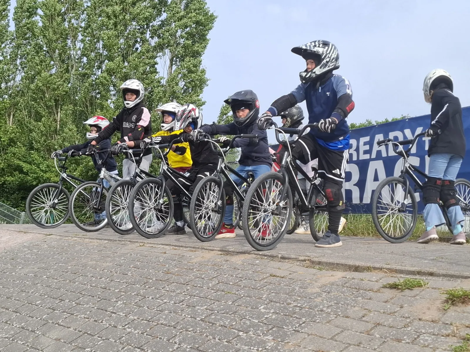 Kindergruppe mit BMX-Rädern und Helmen vor dem READY-TO-RACE-Banner