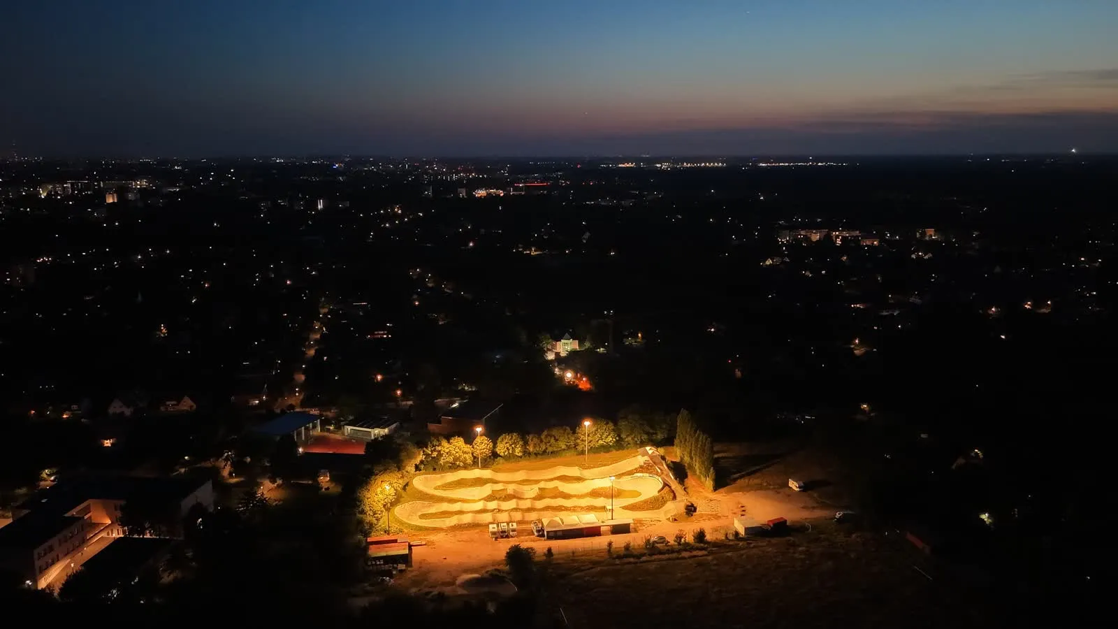 Weiter Blick über Hamburg bei Nacht, in der Mitte leuchtet der BMX-Track im Neusurenland